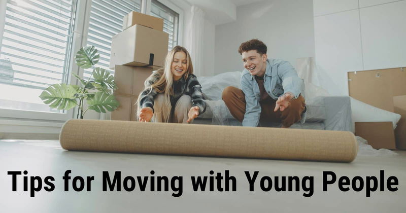 Two young people rolling out an area rug in a new home with boxes in the background