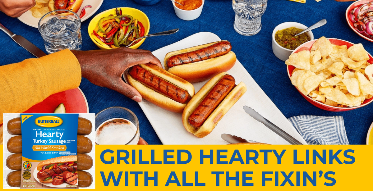 People around a table sharing a meal together with the focus on a plate of Butterball Grilled Hearty Link sausages in hot dog buns.